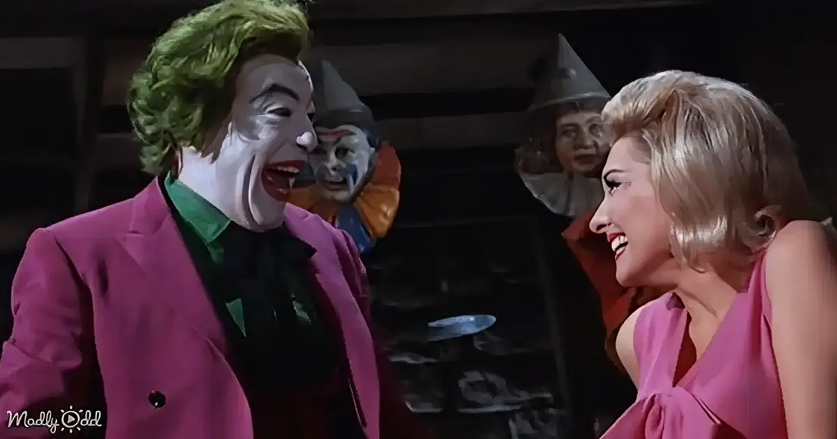 The Joker in a pink suit and green hair laughs with a woman in a pink dress, while a clown head is visible in the background.