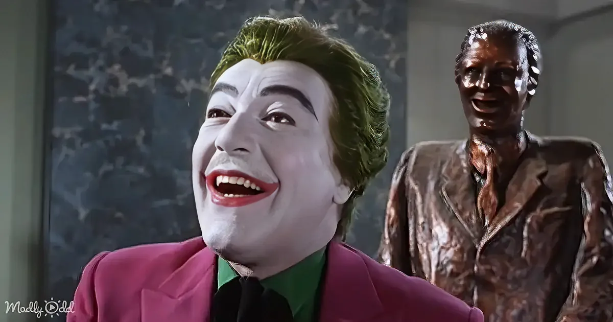 A person in a pink suit with a green shirt and a white face is smiling widely.