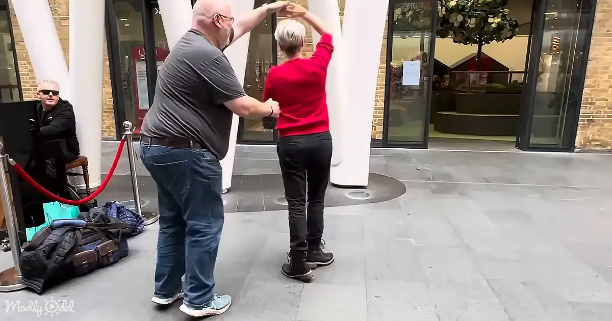 A man and woman are dancing in front of a building with white columns and glass doors.