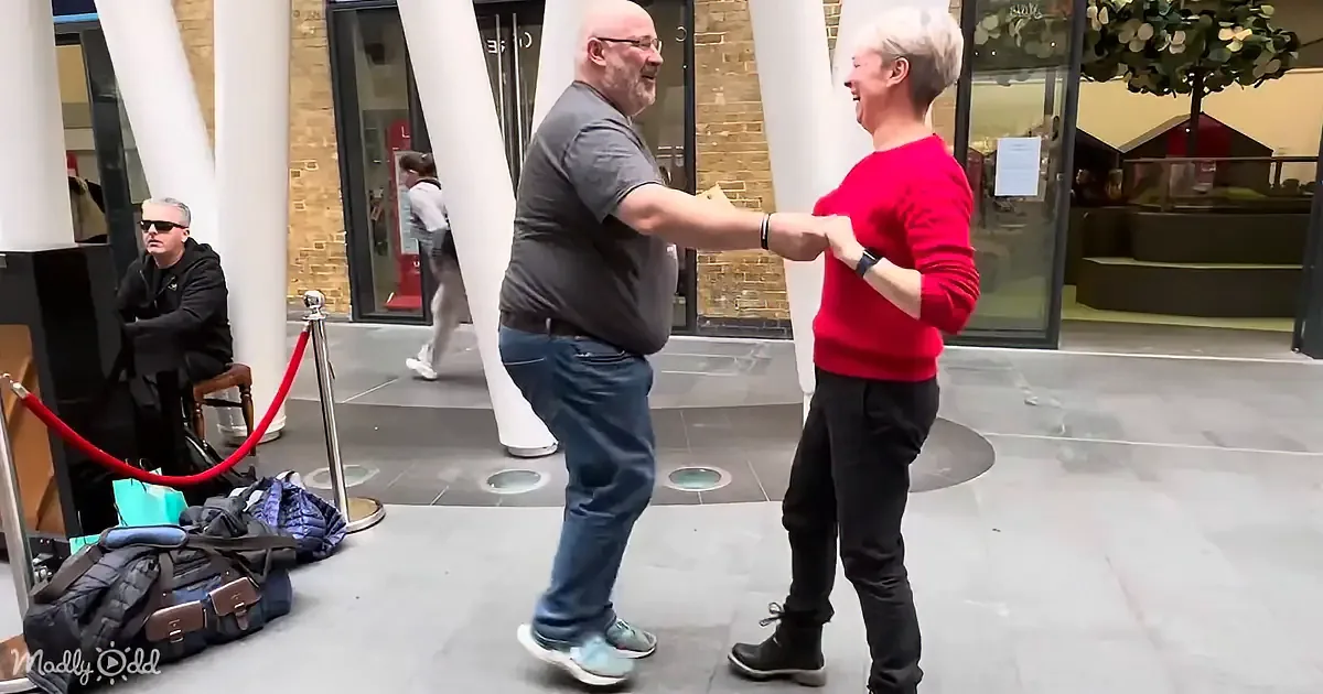 A man and woman are dancing in a public space, surrounded by other people and luggage.
