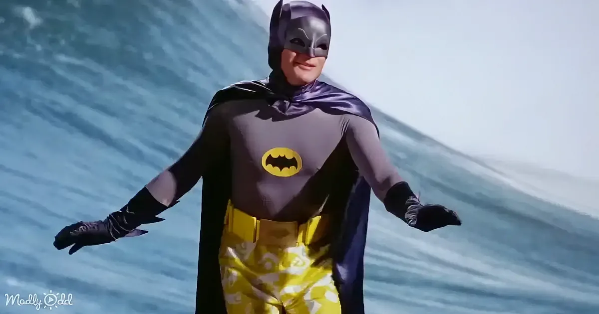 A person in a Batman costume stands with arms outstretched, wearing a purple cape and yellow pants with bat symbols.