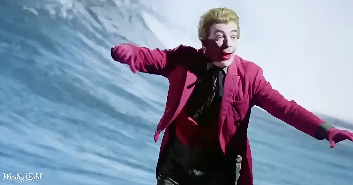 A person in a bright pink suit and green gloves stands with arms outstretched against a snowy backdrop.