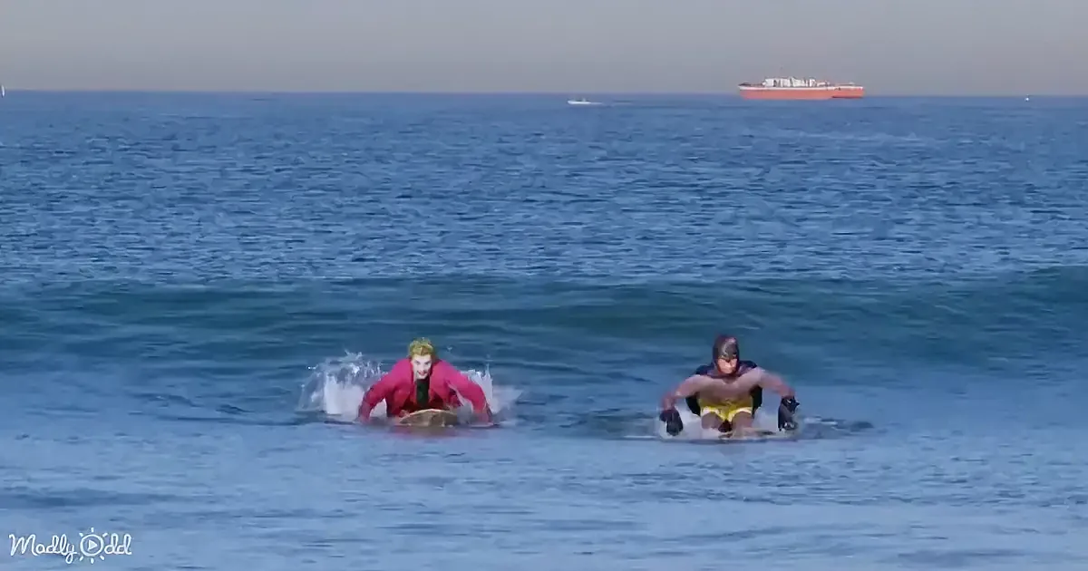 Two people are surfing on small waves in the ocean, wearing colorful wetsuits.