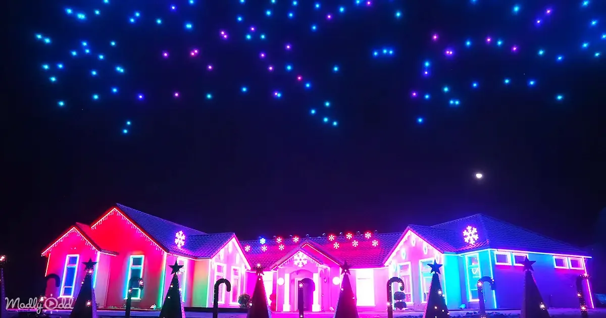 A festive house adorned with colorful lights and Christmas decorations under a night sky with illuminated drones.