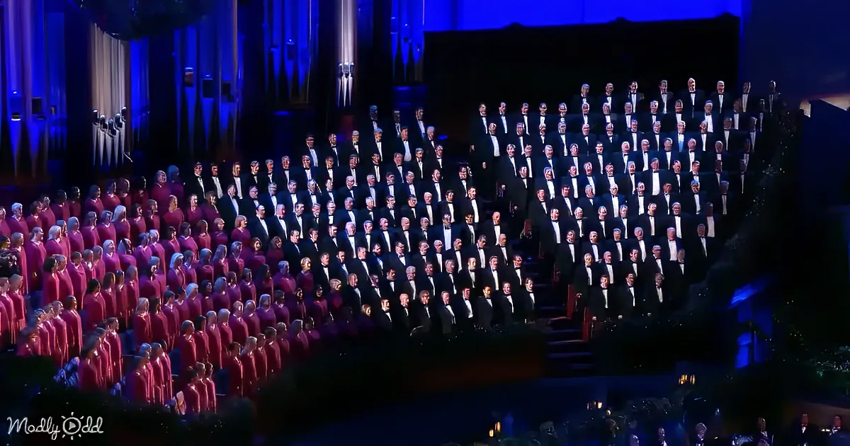 A large choir in formal attire stands in rows on a stage, illuminated by blue lighting.