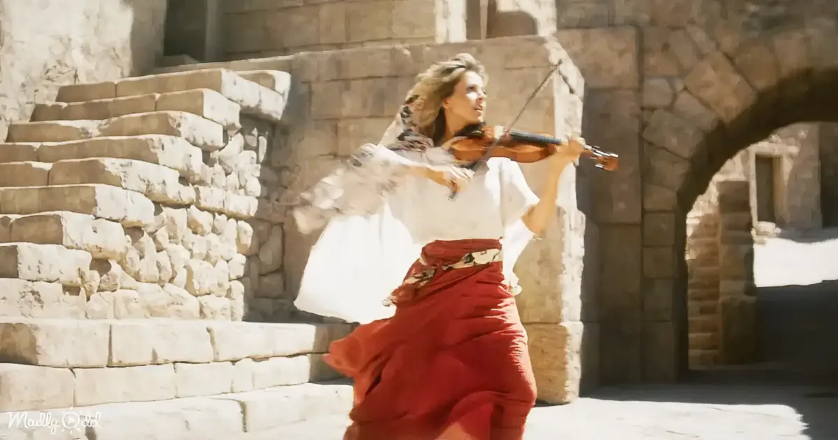A woman in a flowing red skirt and white top plays a violin in front of stone steps and arches.