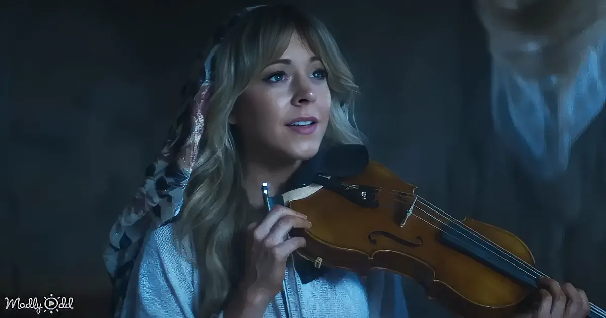 A woman with long blonde hair plays a violin in a dimly lit setting.