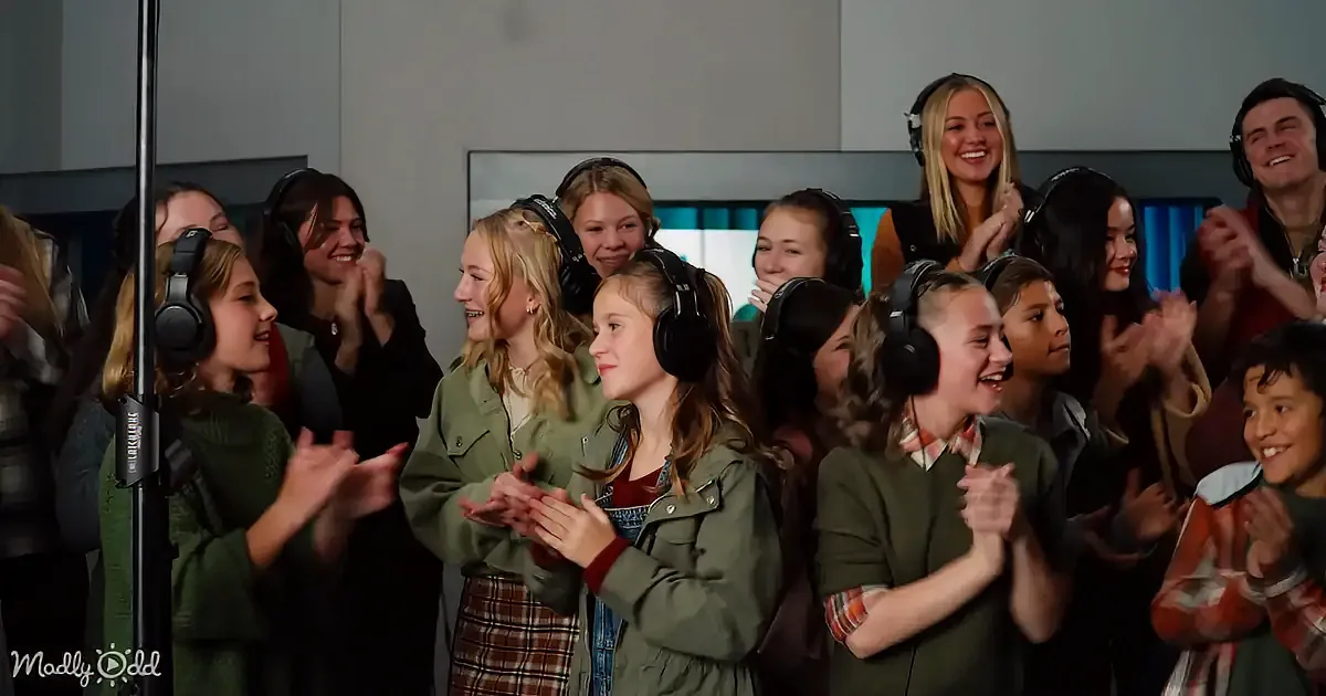 A group of children wearing headphones and clapping, smiling and enjoying themselves in a recording studio.