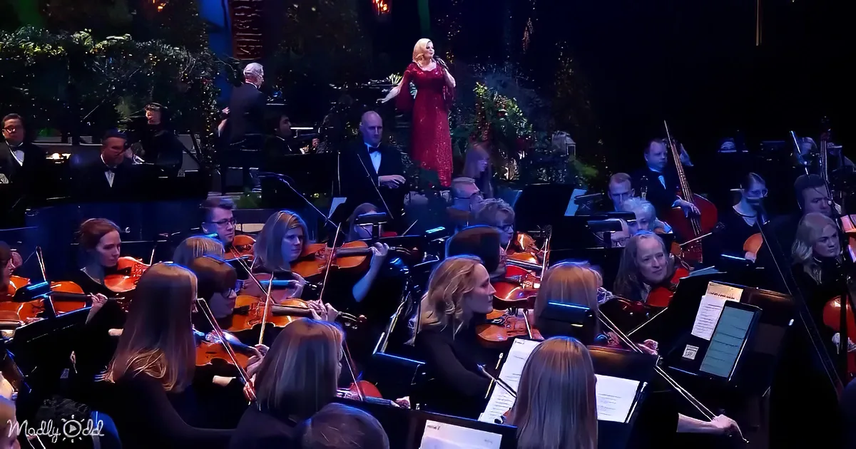 A woman in a red dress sings on stage with an orchestra playing behind her.