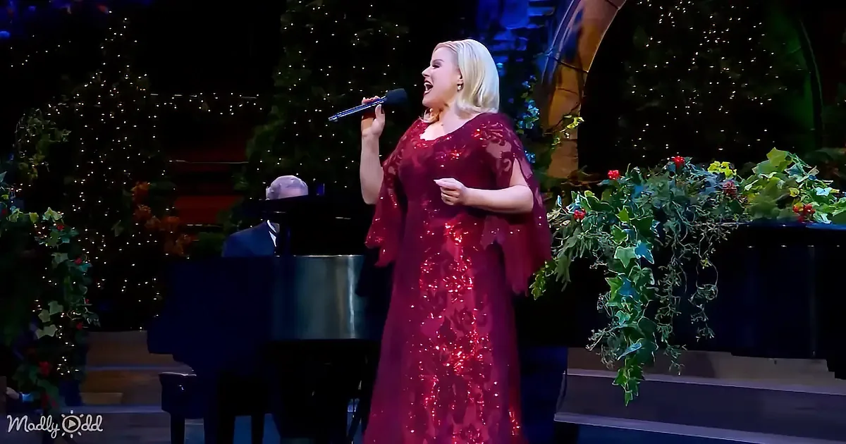 A woman in a red sequined dress sings into a microphone on stage, surrounded by festive decorations.