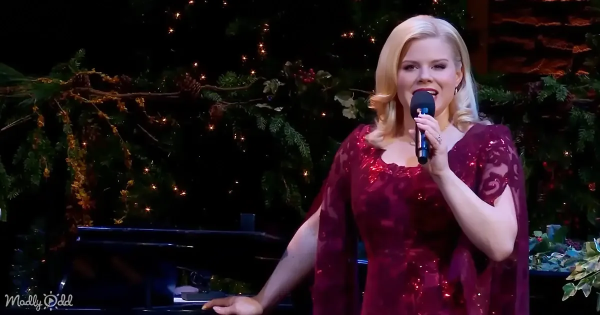 A woman in a sparkly red dress sings into a microphone, with a decorated Christmas tree in the background.