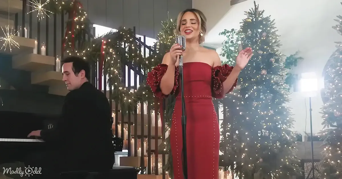 A woman in a red dress sings into a microphone, accompanied by a pianist, with Christmas decorations in the background.