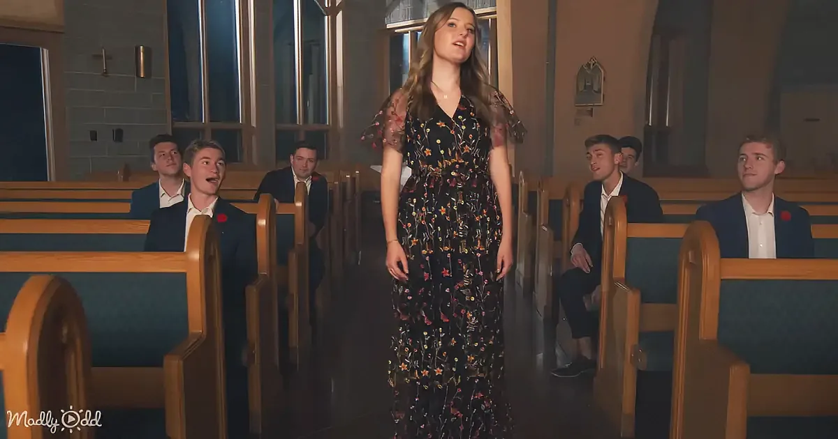 A woman in a floral dress stands in a church aisle, surrounded by seated men in suits.