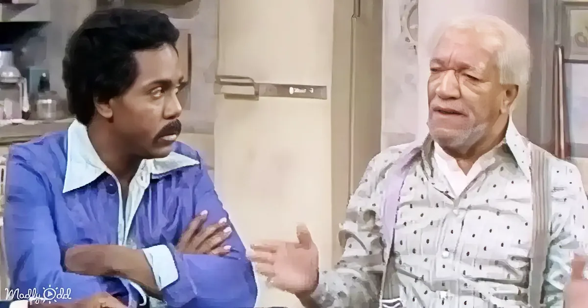 An older man in a polka-dot shirt gestures while talking to a man in a blue jacket with crossed arms.