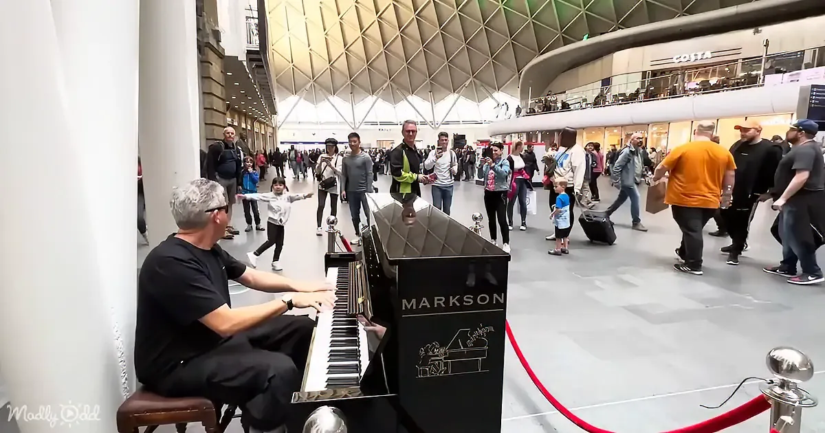 A man plays a Markson piano in a busy station, surrounded by people walking by.