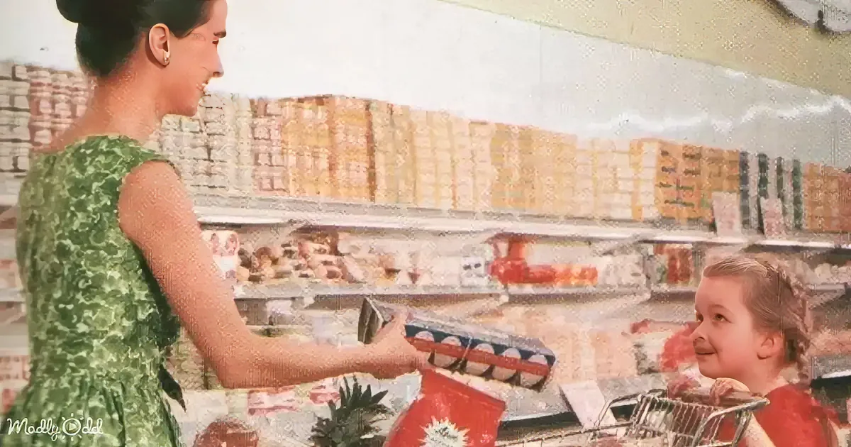 A woman in a green dress hands a carton of eggs to a child in a grocery store aisle.