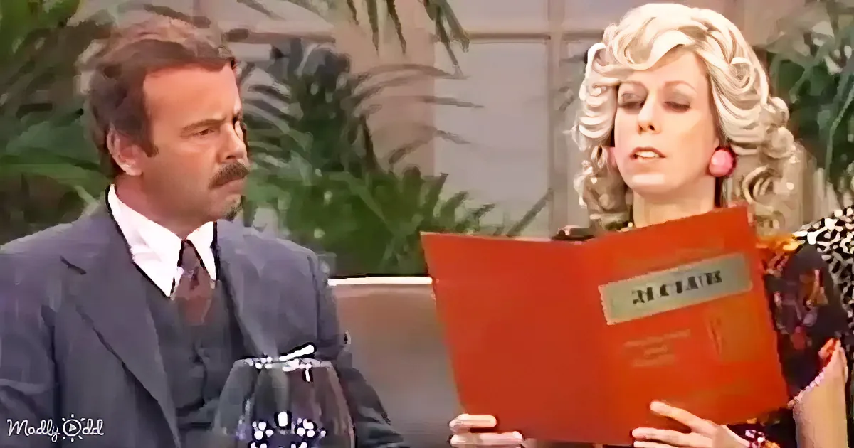 Woman with blonde curls reads a red book, man in suit looks on with a mustache.