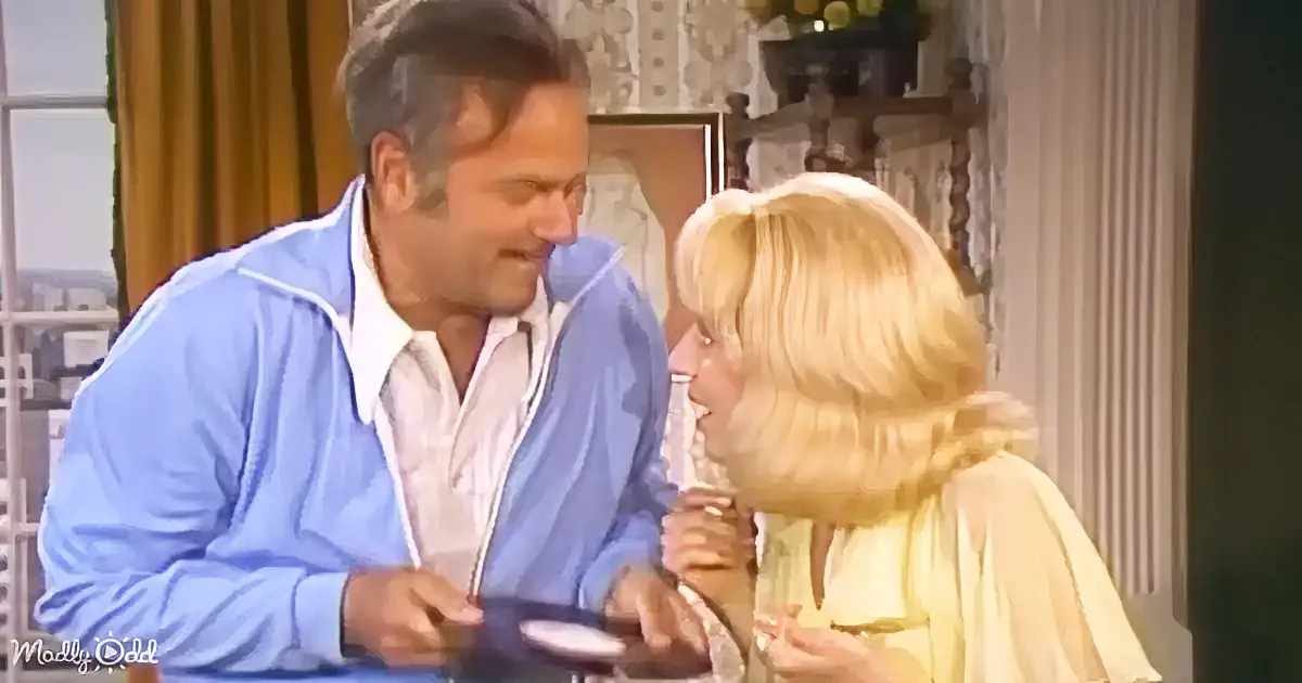 A man in a blue jacket and a woman in a yellow dress are engaged in a conversation, smiling and holding hands.