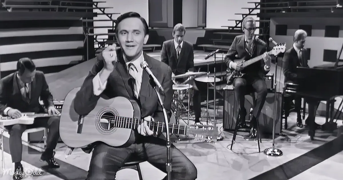 A man in a suit plays guitar and sings on stage with a band.