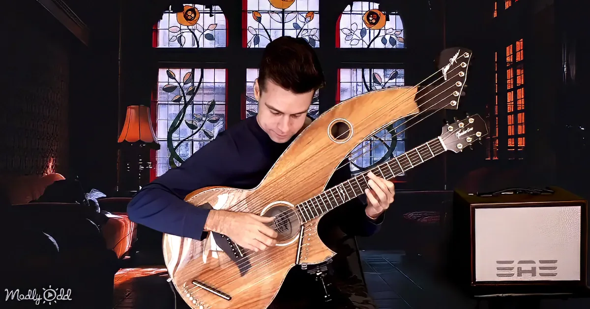 A man plays a unique, wooden guitar with a distinctive shape in a dimly lit room with stained glass windows.