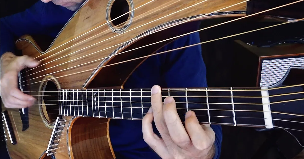A person plays a unique, wooden guitar in a dimly lit room with stained glass windows.