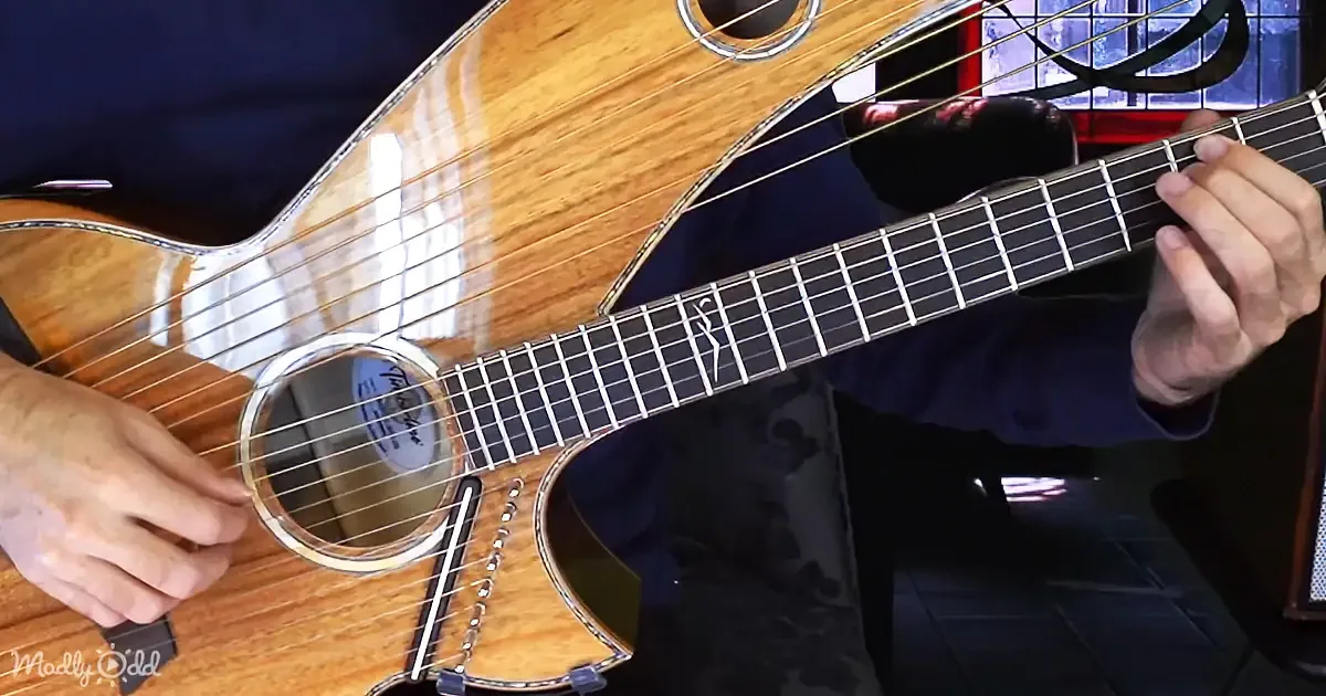 A person plays a wooden acoustic guitar with a left hand on the fretboard and a right hand strumming.