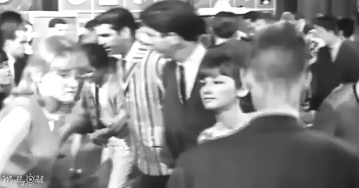 A man in a striped shirt is surrounded by a crowd of people in a busy setting.