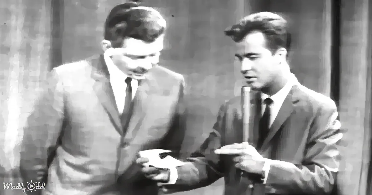 Two men in suits, one blindfolded, both holding objects, possibly in a staged or theatrical setting.