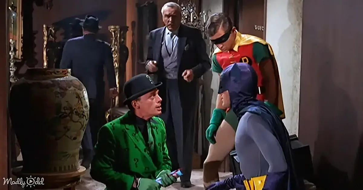 Batman and Robin confront the Riddler in a dramatic scene, with a man in a suit observing.
