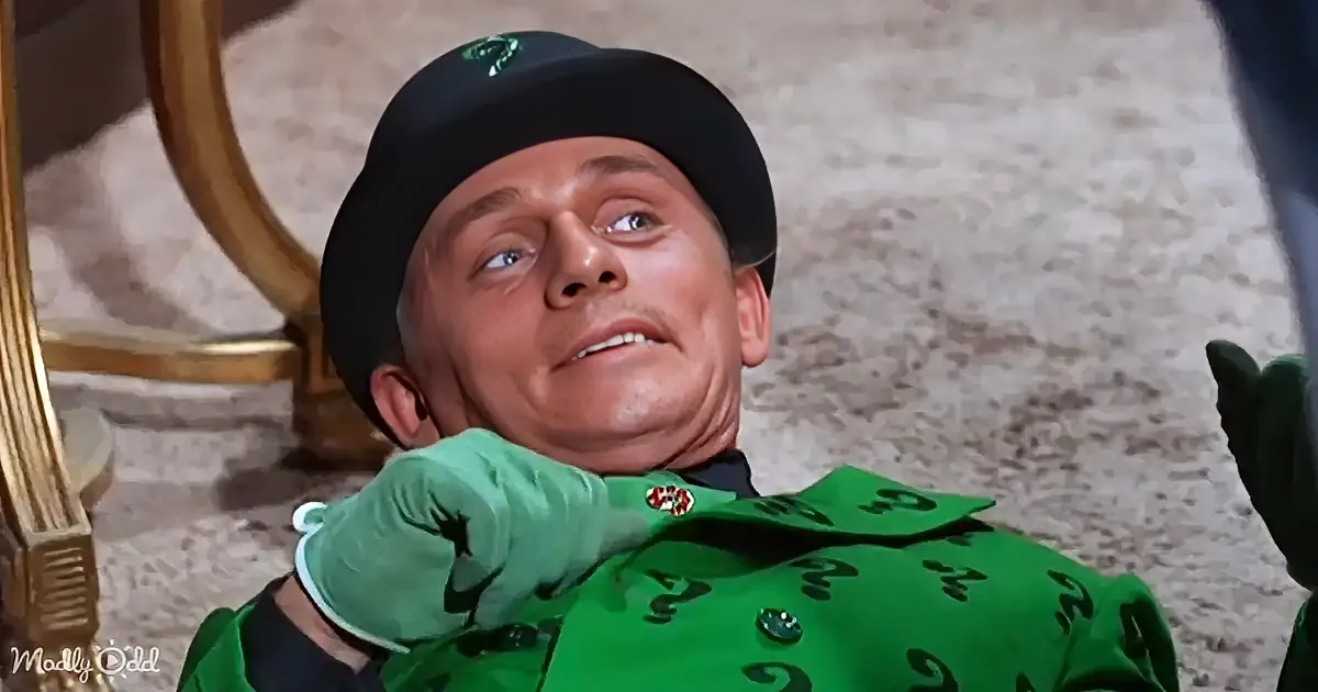 A man in a green suit with question marks and a black hat is looking up with a surprised expression.