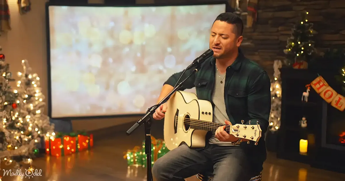 A man plays guitar and sings in front of a Christmas-themed backdrop with lights and decorations.