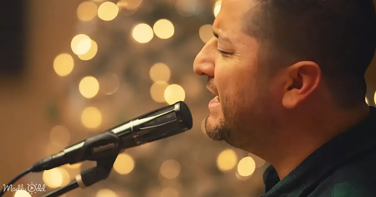 A man sings into a microphone with a blurred background of warm lights.