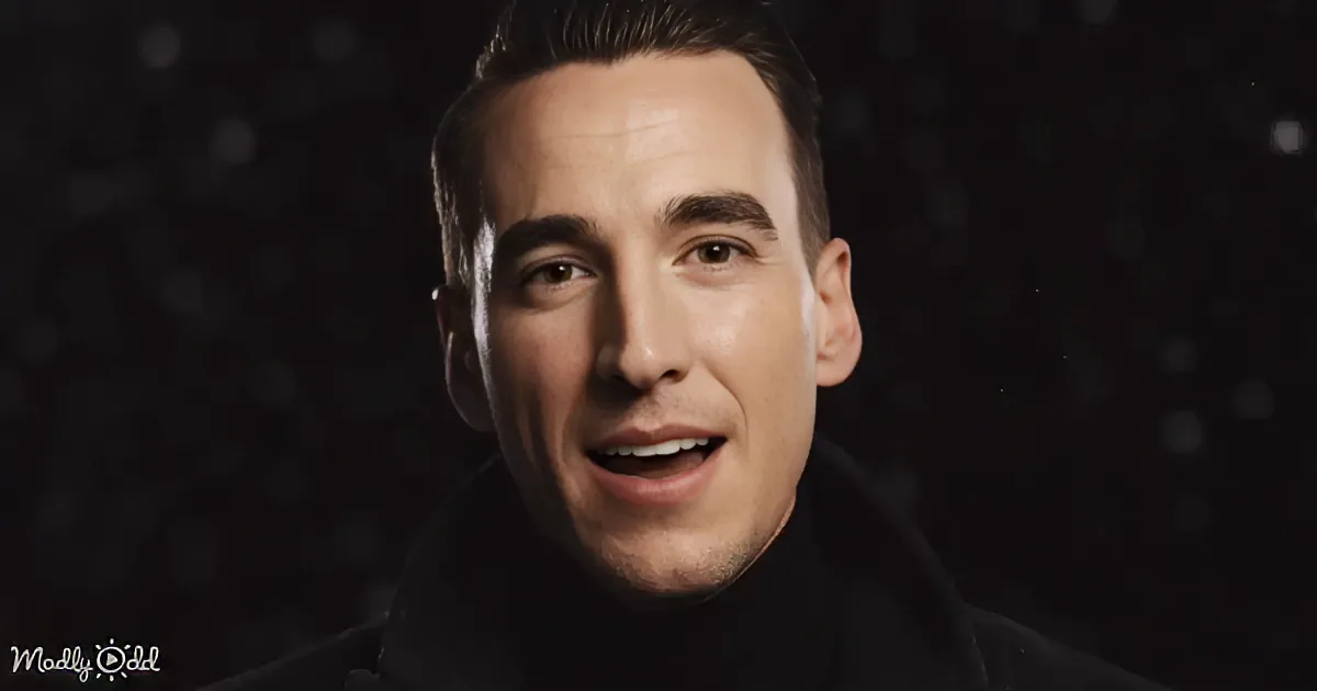 A man with short dark hair, wearing a black top, smiles slightly against a dark, starry background.