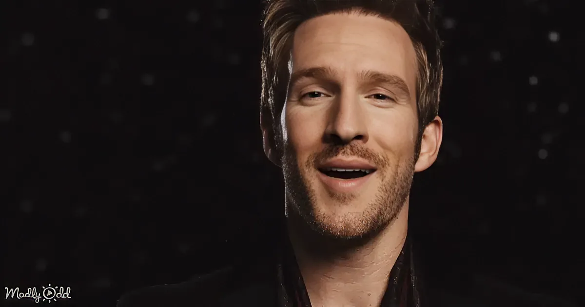 A smiling man with short hair and a beard, wearing a dark jacket, against a dark background with small white dots.