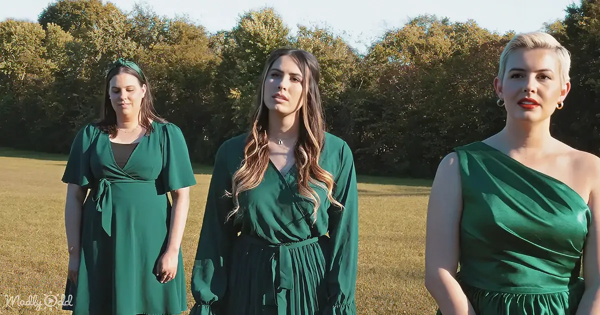 Three women in green dresses stand in a field with trees in the background.