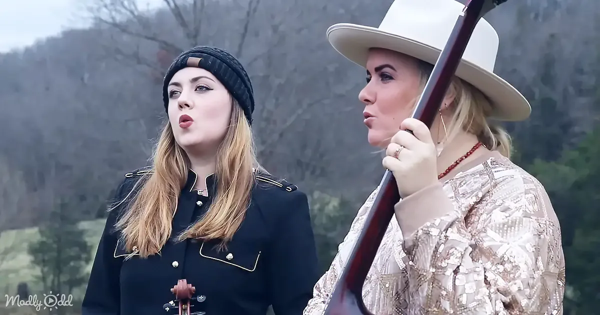 Two women, one in a black outfit and the other in a white hat and patterned shirt, are playing musical instruments outdoors.