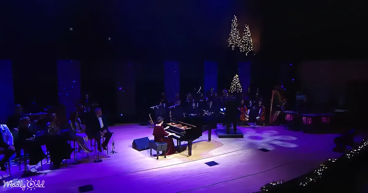 A pianist in red plays on stage with an orchestra and Christmas trees in the background.