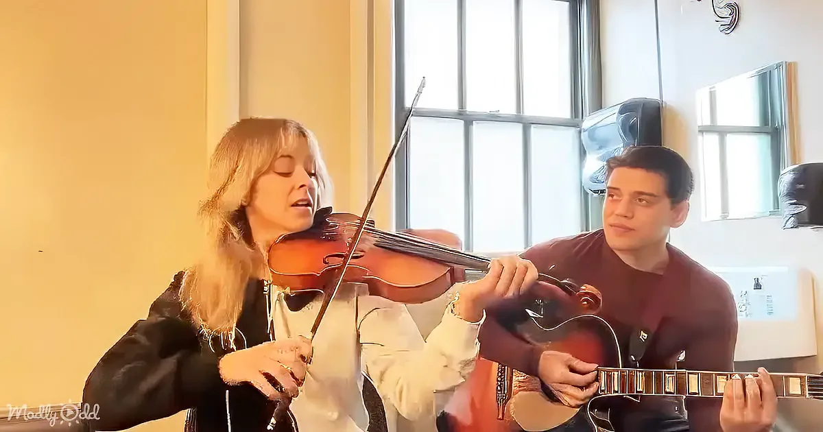 A woman plays violin while a man plays guitar, both focused on their instruments.