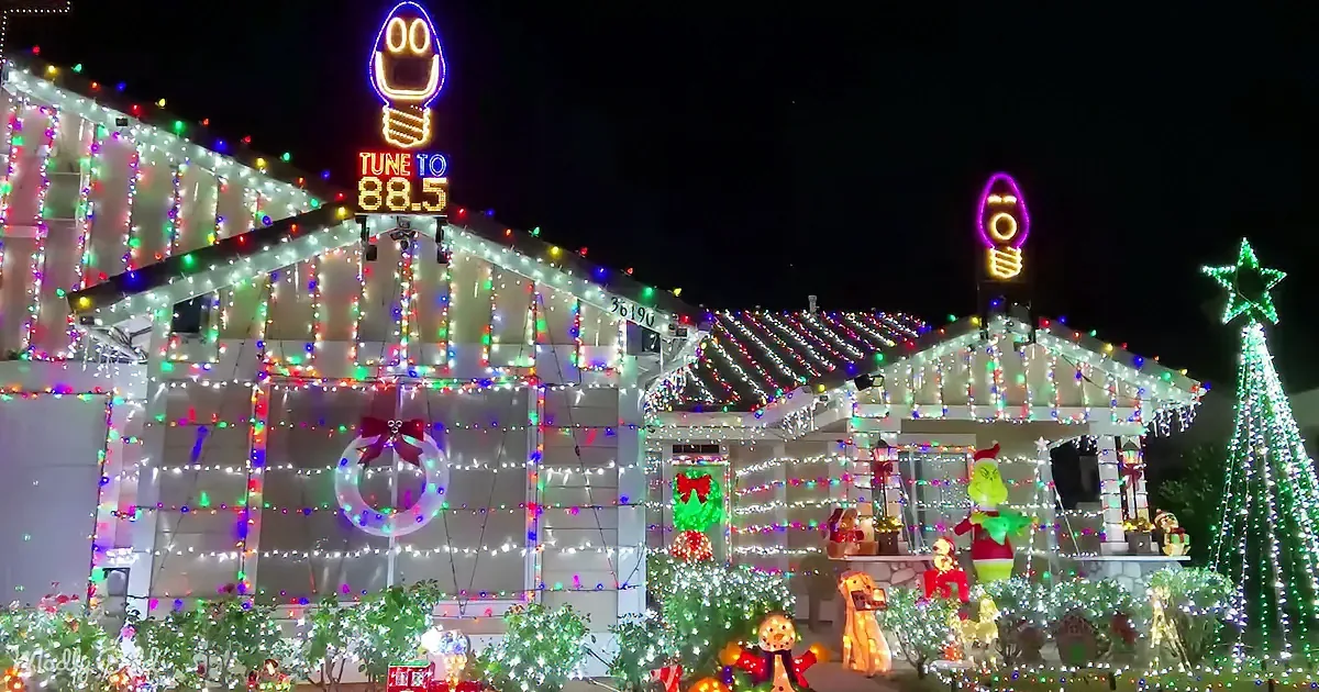 A house adorned with festive Christmas lights and decorations, including a Grinch figure and a light bulb sign.