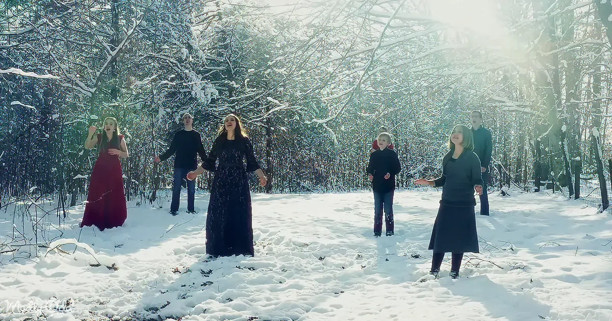 A group of people singing in a snowy forest, surrounded by snow-covered trees.