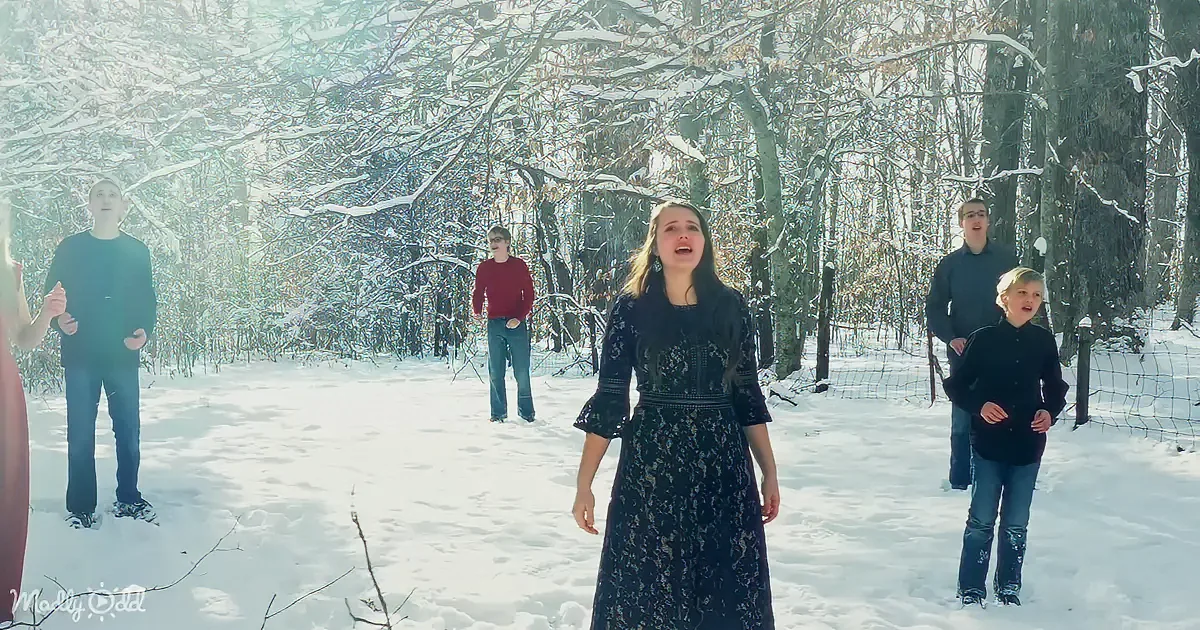 A woman in a dark dress sings in a snowy forest with four others.