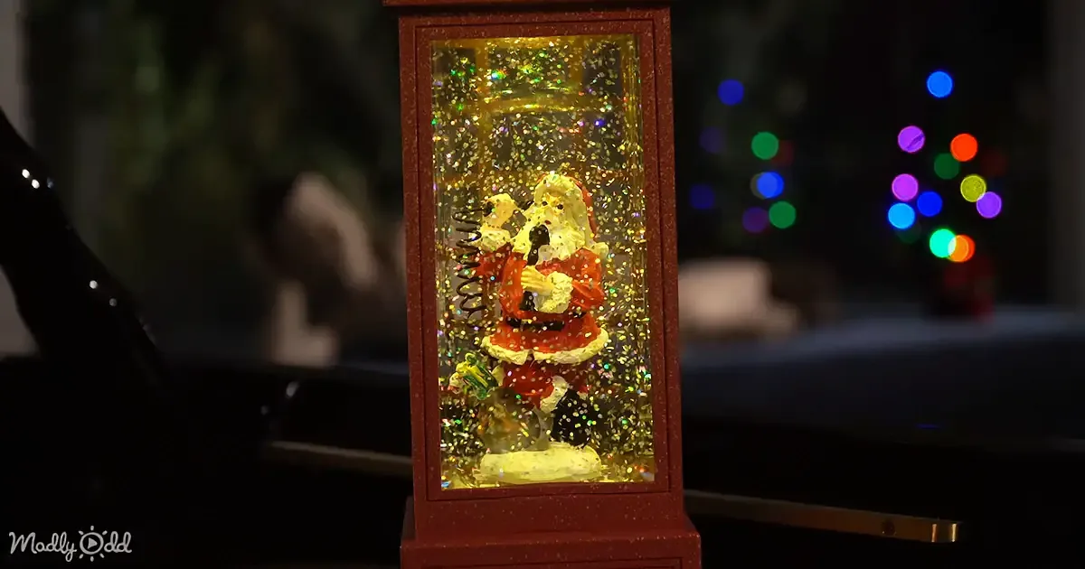A festive Santa figurine inside a glittery lantern, surrounded by colorful lights in the background.
