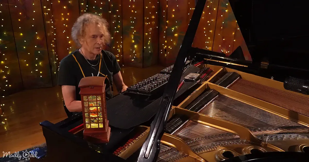 A man sits at a grand piano with an open lid, surrounded by festive lights.