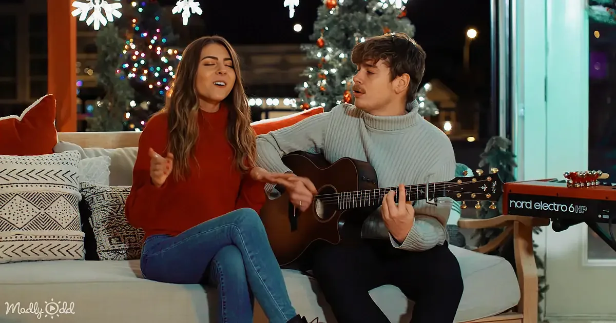 A couple sings and plays guitar on a couch, surrounded by Christmas lights and decorations.