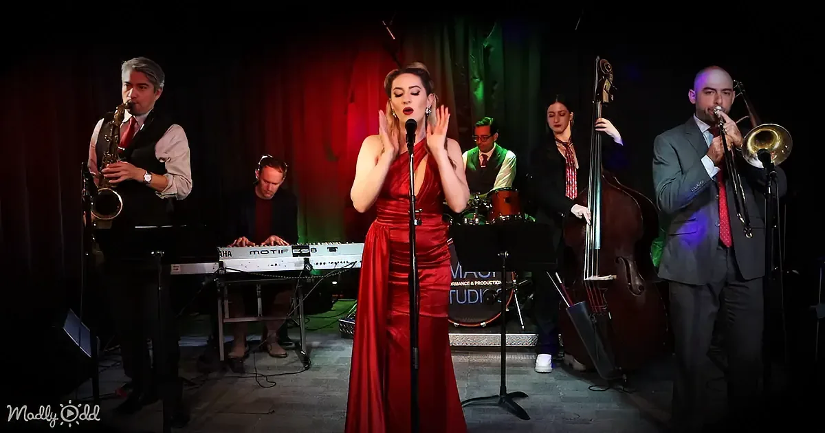 A woman in a red dress sings passionately on stage with a band playing instruments.