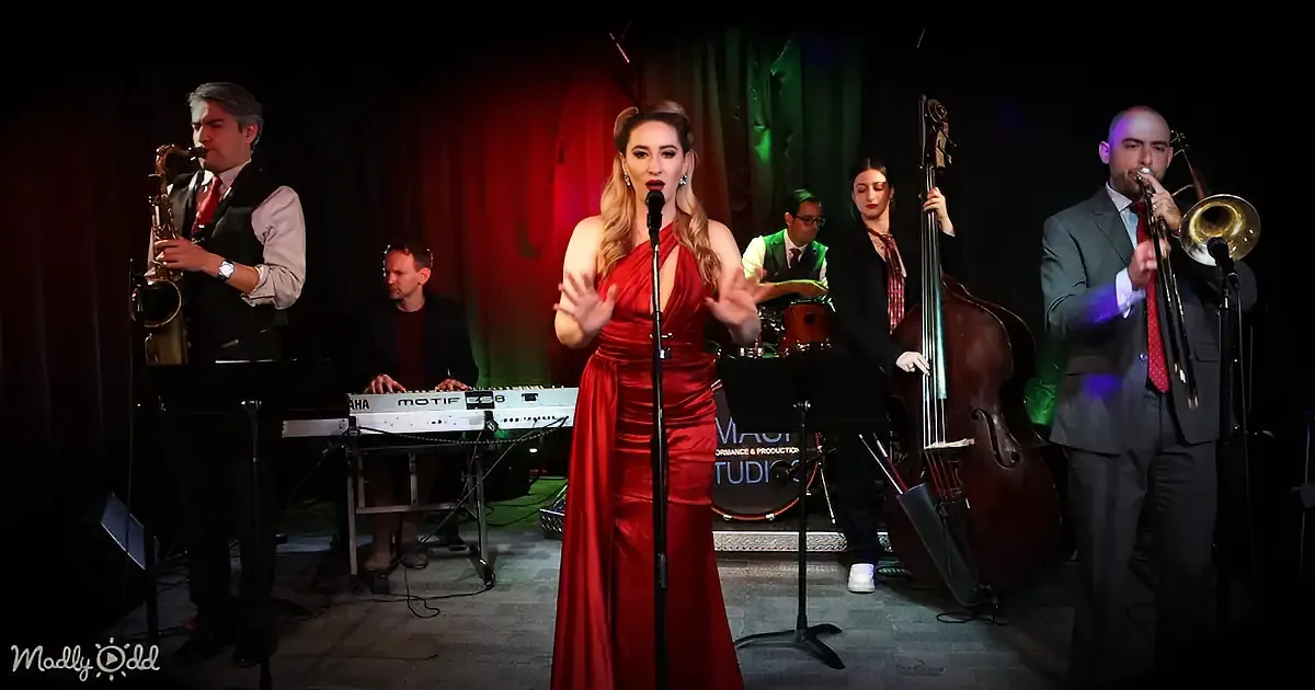 A woman in a red dress sings into a microphone, surrounded by a band playing instruments.