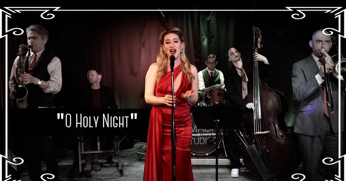A woman in a red dress sings into a microphone on stage with a band.