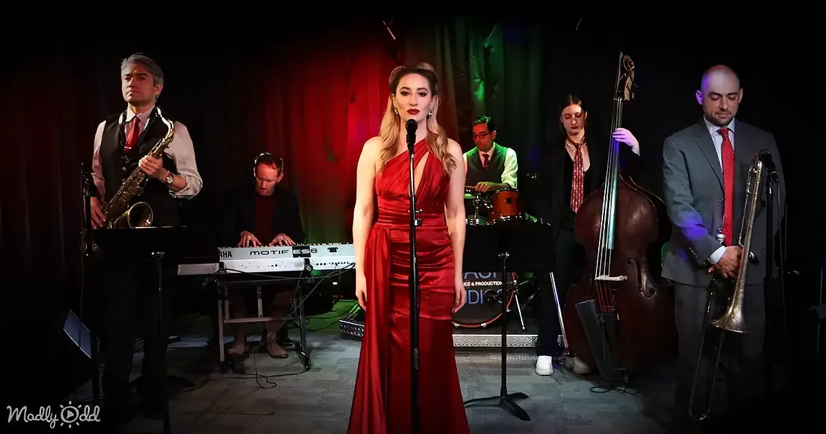 A woman in a red dress sings into a microphone, surrounded by a band playing instruments.