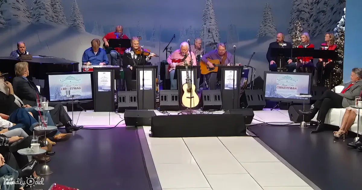 A band performs on stage with a winter backdrop, surrounded by audience members and monitors.