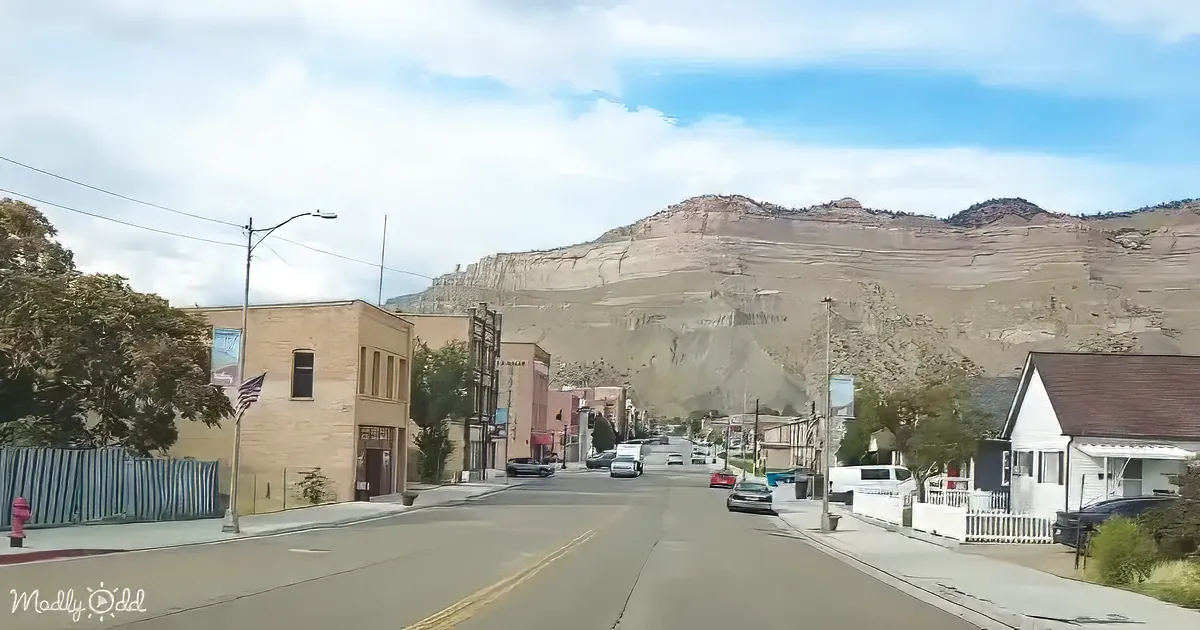 A small town street with a mountain in the background, cars parked, and a clear sky.